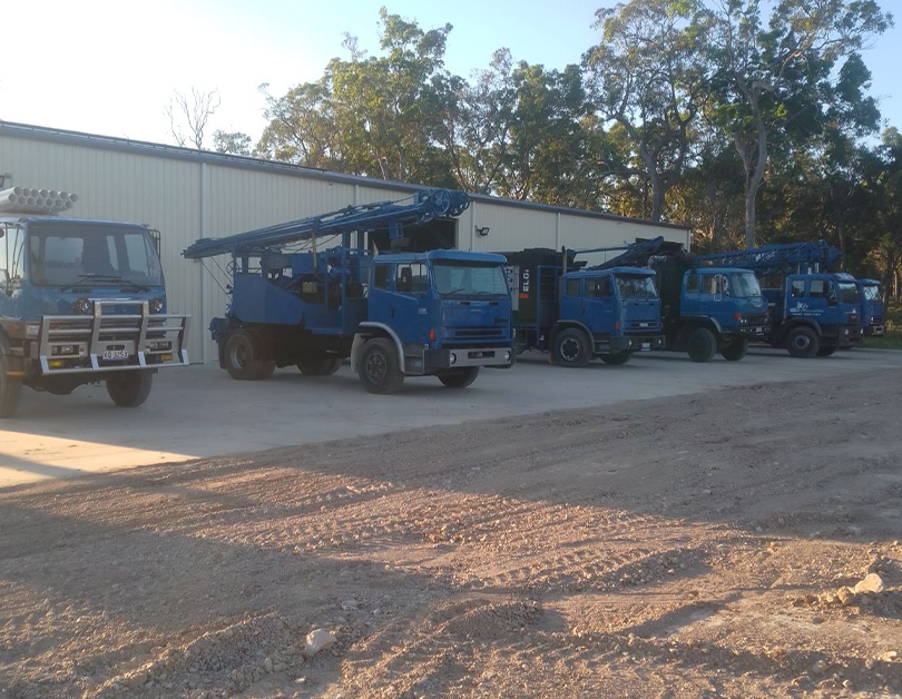 Four Blue Utility Trucks with Cranes Parked Outside a Warehouse Surrounded by Trees — Bore Drilling in Bundaberg, QLD